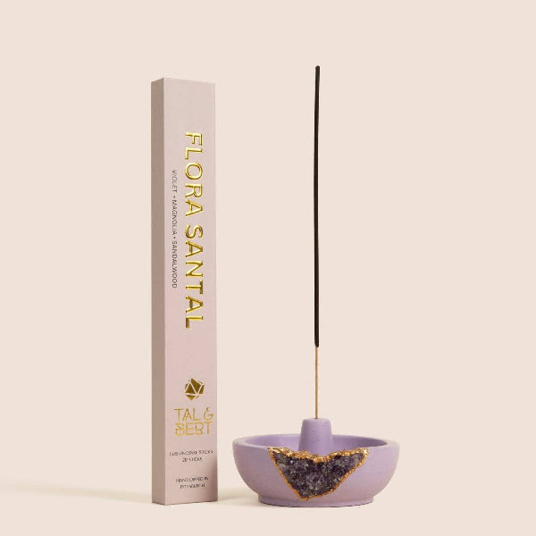 Purple incense holder with a single black incense stick next to its packaging on a beige background