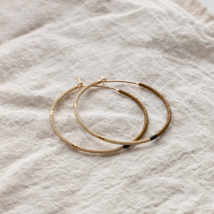 Set of three gold hoop earrings with black accents on a textured beige fabric background