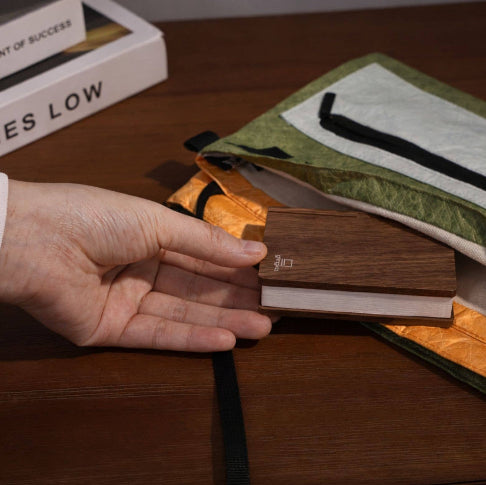 Hand holding a wooden item next to a green pouch on a wooden surface