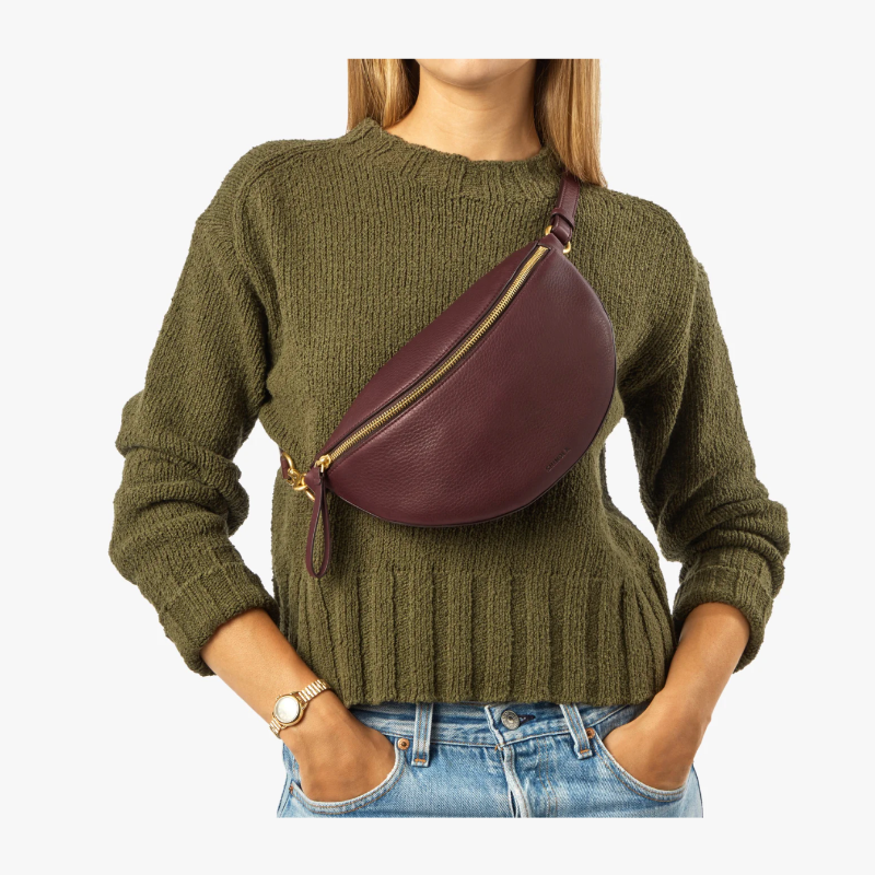 Person wearing a green sweater with a burgundy leather fanny pack on a white background